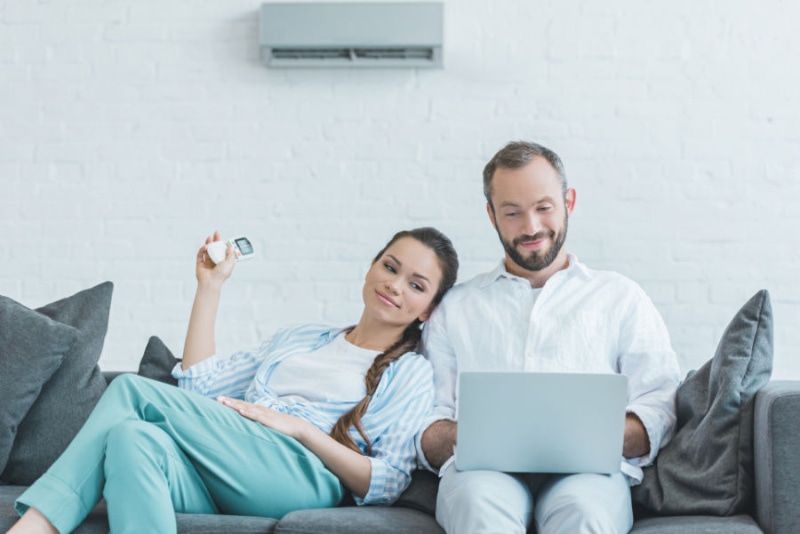 a man and woman sitting on a couch with a laptop, sitting below ductless unit.