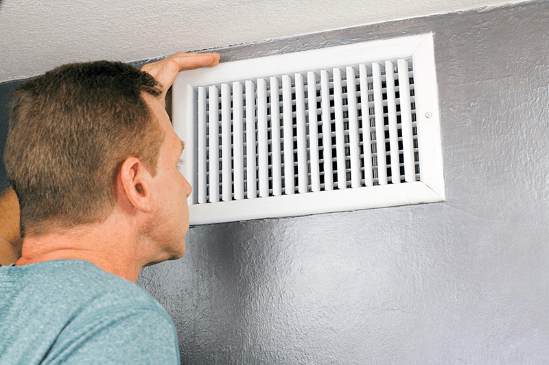man looking into the air duct in his home