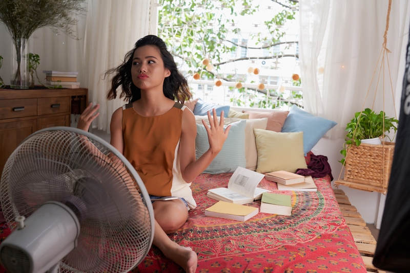 Sweating Asian girl cooling herself with big fan. She needs a new ac