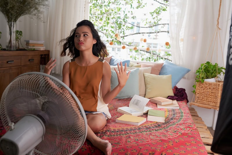 Sweating Asian girl cooling herself with big fan. She needs a new ac